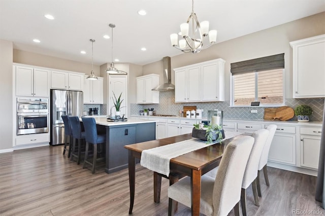 kitchen with white cabinets, a kitchen island, stainless steel appliances, light countertops, and wall chimney range hood