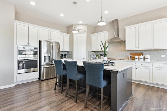 kitchen featuring wall chimney range hood, an island with sink, dark wood finished floors, and appliances with stainless steel finishes