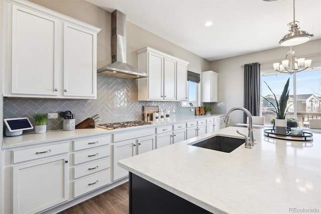 kitchen featuring decorative backsplash, dark wood-type flooring, white cabinets, a sink, and wall chimney range hood