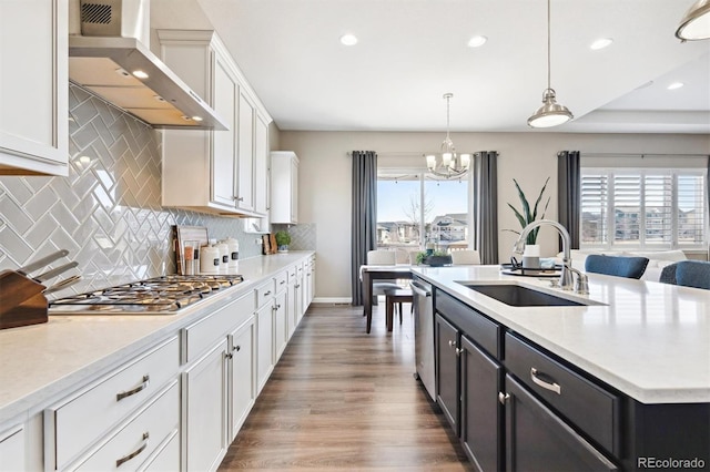 kitchen with stainless steel appliances, light countertops, white cabinets, a sink, and wall chimney exhaust hood