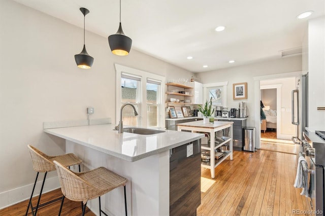 kitchen featuring light wood finished floors, open shelves, a sink, a peninsula, and a kitchen breakfast bar