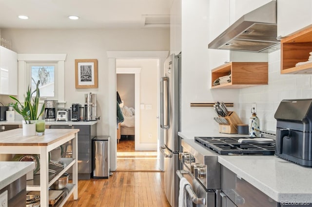 kitchen with light wood-style flooring, stainless steel appliances, decorative backsplash, wall chimney exhaust hood, and modern cabinets