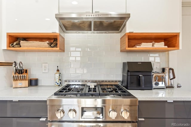 kitchen featuring gas range, light stone countertops, under cabinet range hood, open shelves, and backsplash