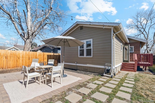 back of property featuring brick siding, outdoor dining space, a patio area, fence, and a wooden deck