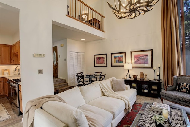 living area featuring stairs, light wood-type flooring, a high ceiling, and an inviting chandelier