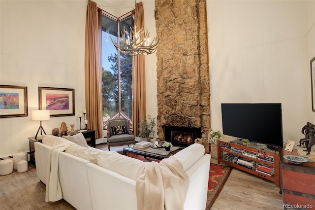 living room featuring a baseboard radiator, a stone fireplace, a high ceiling, and wood finished floors