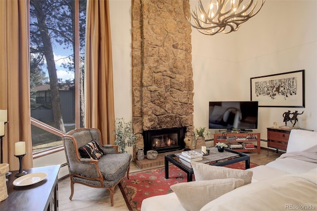 living room featuring wood finished floors, an inviting chandelier, baseboard heating, a stone fireplace, and a wealth of natural light