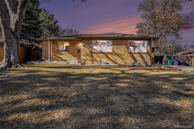 back of house at dusk with a yard, brick siding, and fence