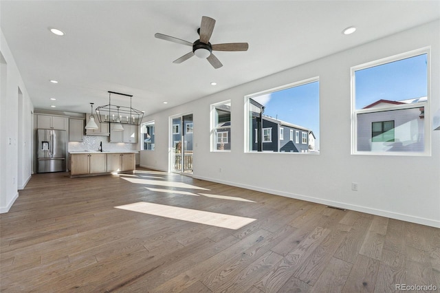 unfurnished living room featuring ceiling fan with notable chandelier and light hardwood / wood-style flooring