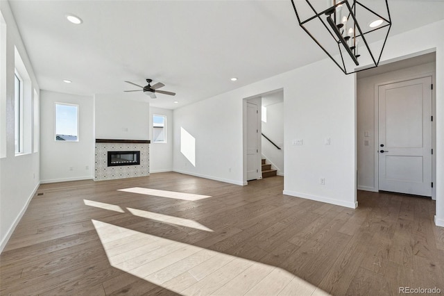 unfurnished living room with ceiling fan with notable chandelier, light wood-type flooring, and a tile fireplace