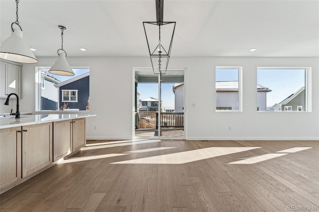 kitchen with light brown cabinetry, light wood-type flooring, hanging light fixtures, and sink