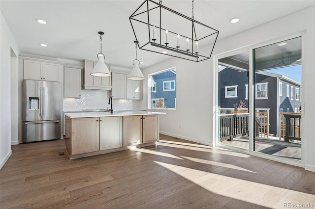 kitchen featuring a kitchen island with sink, stainless steel refrigerator with ice dispenser, dark hardwood / wood-style floors, decorative backsplash, and decorative light fixtures