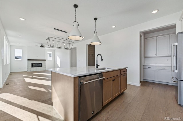 kitchen with a center island with sink, sink, decorative light fixtures, light hardwood / wood-style floors, and stainless steel appliances