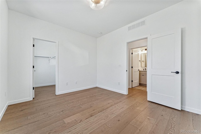 unfurnished bedroom with light wood-type flooring, a walk in closet, and a closet