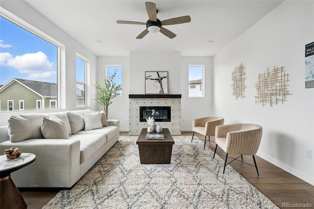 living room featuring a glass covered fireplace, ceiling fan, baseboards, and wood finished floors