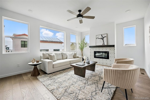 living area featuring visible vents, a ceiling fan, a glass covered fireplace, wood finished floors, and baseboards