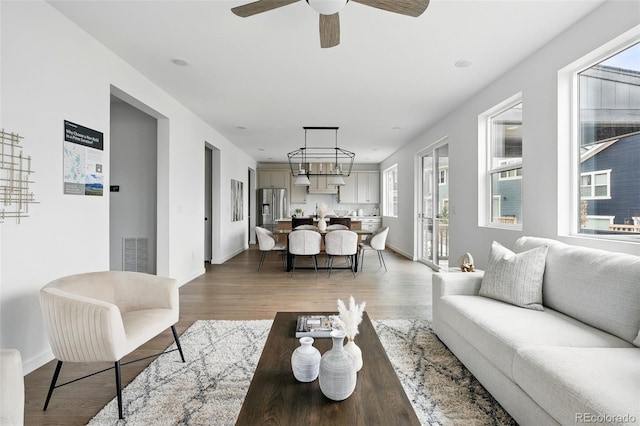 living area with ceiling fan, wood finished floors, visible vents, and baseboards