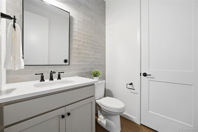 half bathroom featuring vanity, wood finished floors, tile walls, toilet, and backsplash