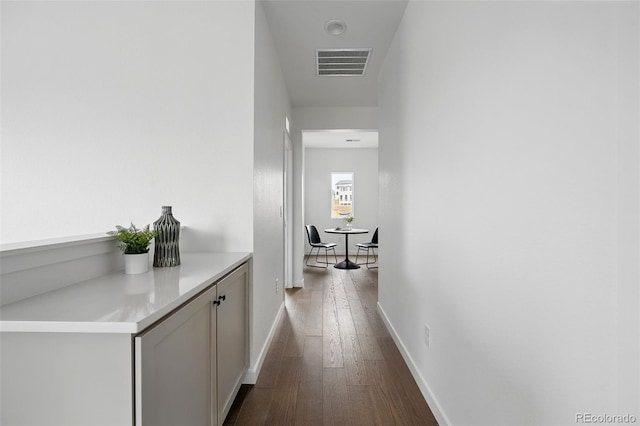 hall featuring visible vents, dark wood-type flooring, and baseboards