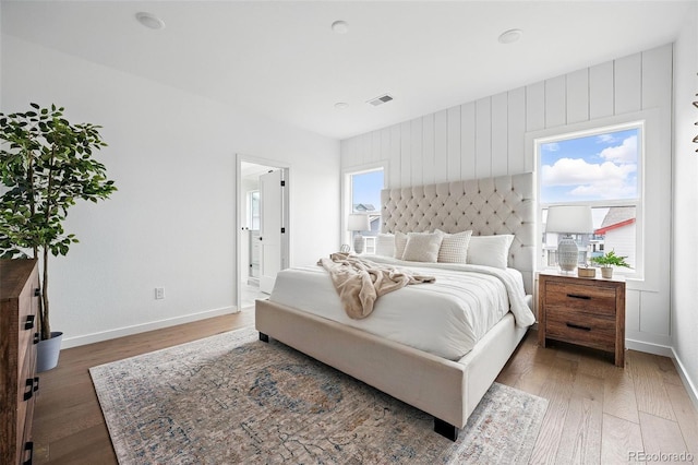 bedroom with multiple windows, wood finished floors, visible vents, and baseboards