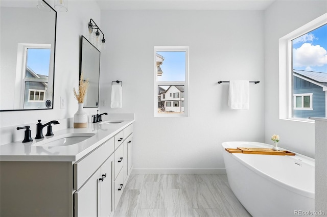 full bath featuring double vanity, a soaking tub, baseboards, and a sink