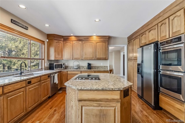 2154 S Parfet Dr, Lakewood, CO 80227 - kitchen featuring appliances with stainless steel finishes, a sink, light wood-type flooring, light stone countertops, and a center island