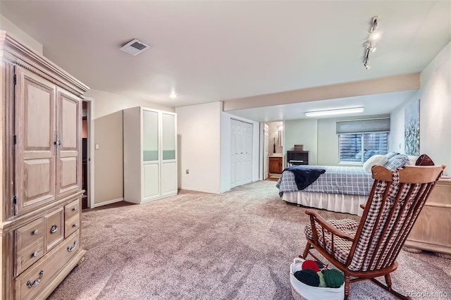 bedroom with visible vents, light carpet, ensuite bath, and track lighting