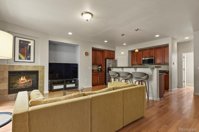 living room featuring light wood-style flooring, recessed lighting, a tiled fireplace, and baseboards