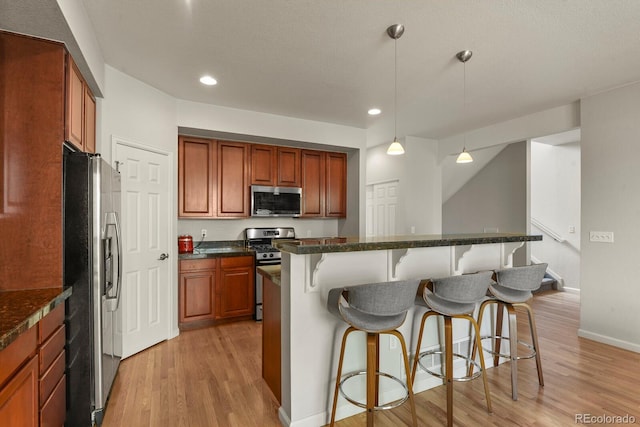 kitchen featuring appliances with stainless steel finishes, a kitchen bar, light wood finished floors, decorative light fixtures, and recessed lighting