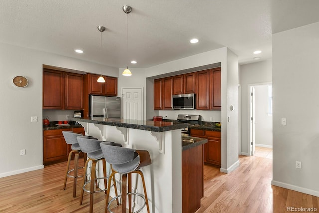 kitchen featuring stainless steel appliances, a kitchen bar, light wood-style floors, dark countertops, and a center island