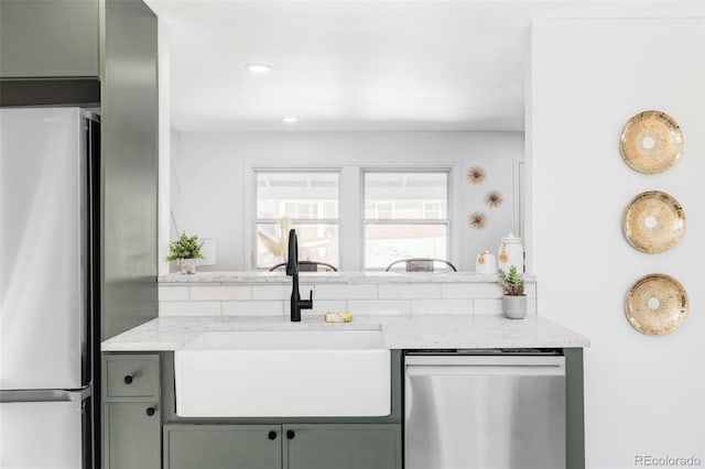 kitchen featuring appliances with stainless steel finishes, sink, green cabinets, and light stone counters