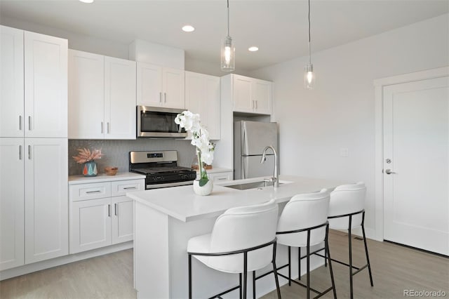 kitchen with a kitchen island with sink, white cabinets, stainless steel appliances, and decorative light fixtures