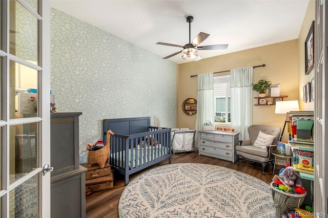 bedroom with ceiling fan, dark hardwood / wood-style floors, and a nursery area