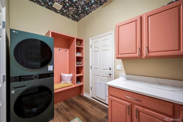 clothes washing area with dark hardwood / wood-style flooring, stacked washer and dryer, and cabinets