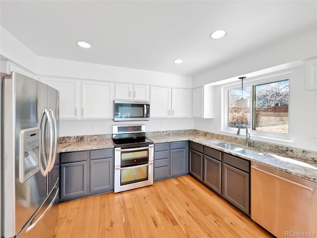 kitchen featuring white cabinets, appliances with stainless steel finishes, light stone counters, light wood-style floors, and a sink