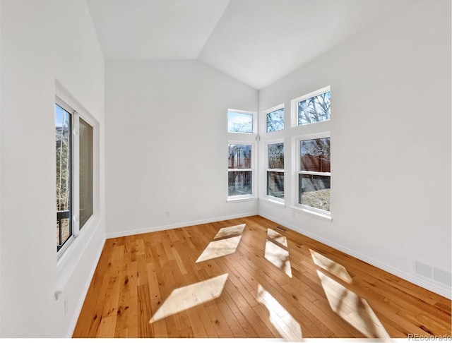 empty room featuring high vaulted ceiling, wood-type flooring, visible vents, and baseboards