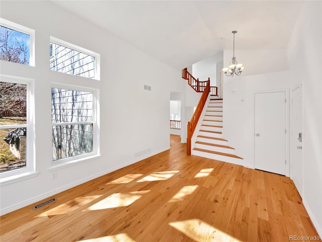 entrance foyer with high vaulted ceiling, stairway, a chandelier, and hardwood / wood-style floors