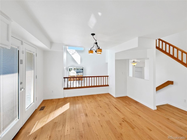 unfurnished room featuring visible vents, baseboards, stairway, light wood-style floors, and a notable chandelier