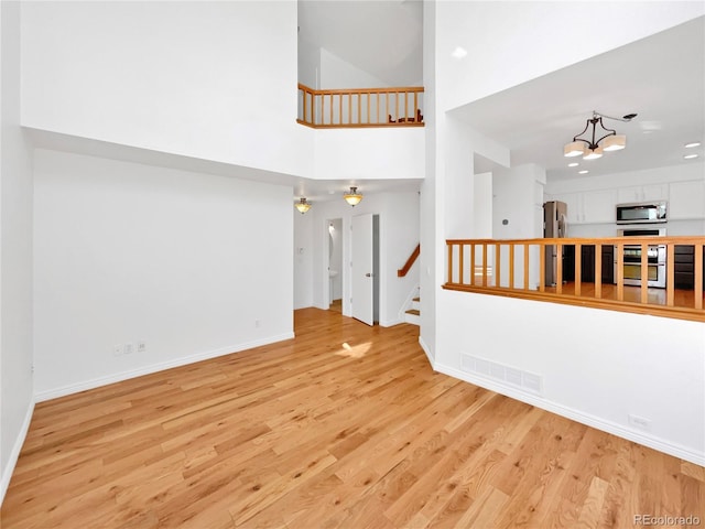 empty room with a chandelier, visible vents, baseboards, stairs, and light wood finished floors