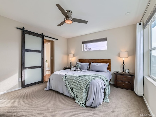 bedroom featuring a ceiling fan, baseboards, carpet floors, ensuite bath, and a barn door