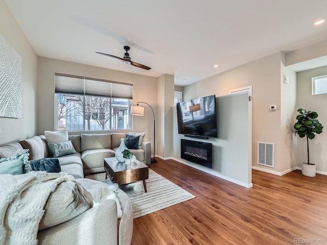 living area with a glass covered fireplace, wood finished floors, visible vents, and baseboards