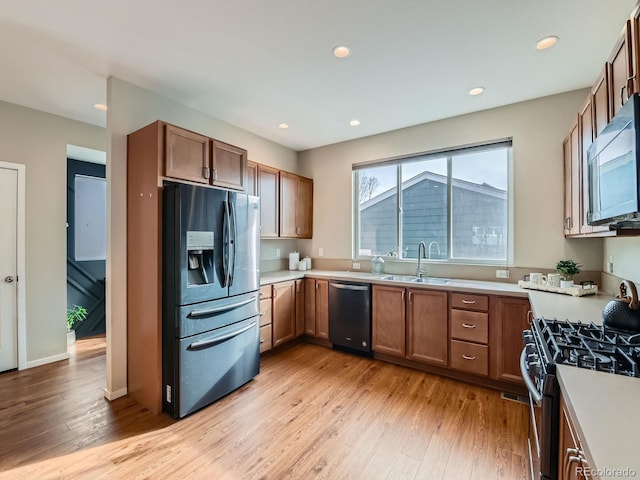 kitchen featuring light wood-style flooring, a sink, appliances with stainless steel finishes, brown cabinetry, and light countertops