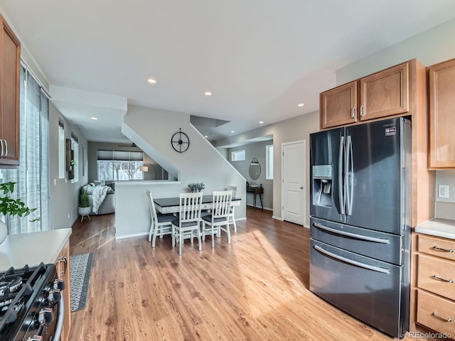 kitchen with light wood-style flooring, stainless steel refrigerator with ice dispenser, recessed lighting, light countertops, and gas range