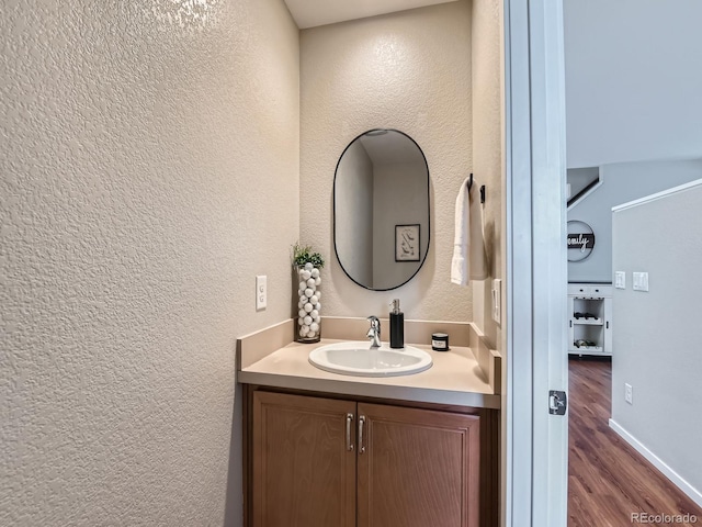 bathroom with baseboards, vanity, a textured wall, and wood finished floors