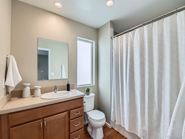 full bathroom featuring toilet, vanity, a textured wall, and wood finished floors