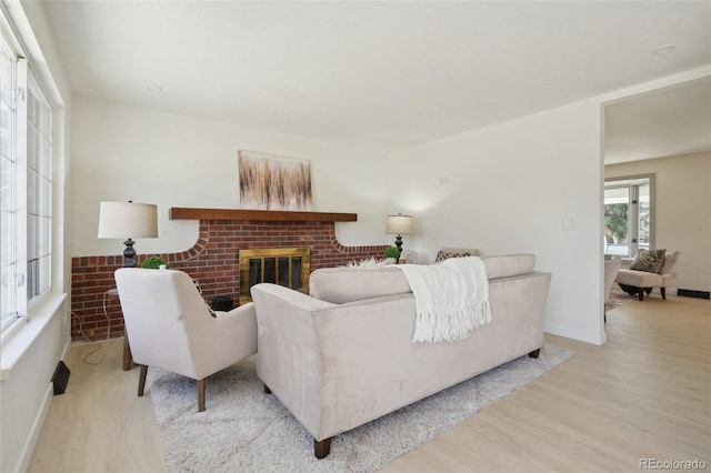 living area with baseboards, a brick fireplace, and light wood-style flooring
