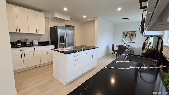 kitchen featuring stainless steel fridge, light wood-style flooring, dark countertops, and white cabinetry