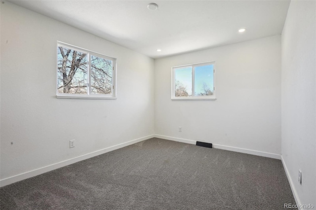 empty room with a healthy amount of sunlight, baseboards, and dark carpet