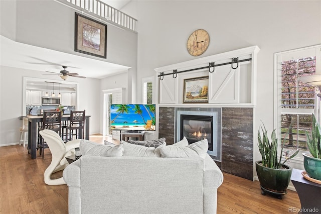 living room featuring ceiling fan, wood-type flooring, a tiled fireplace, and a towering ceiling