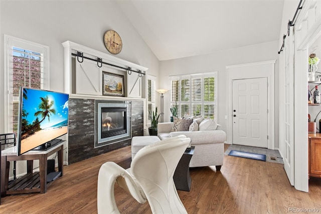 living room featuring high vaulted ceiling, a barn door, hardwood / wood-style floors, and a fireplace